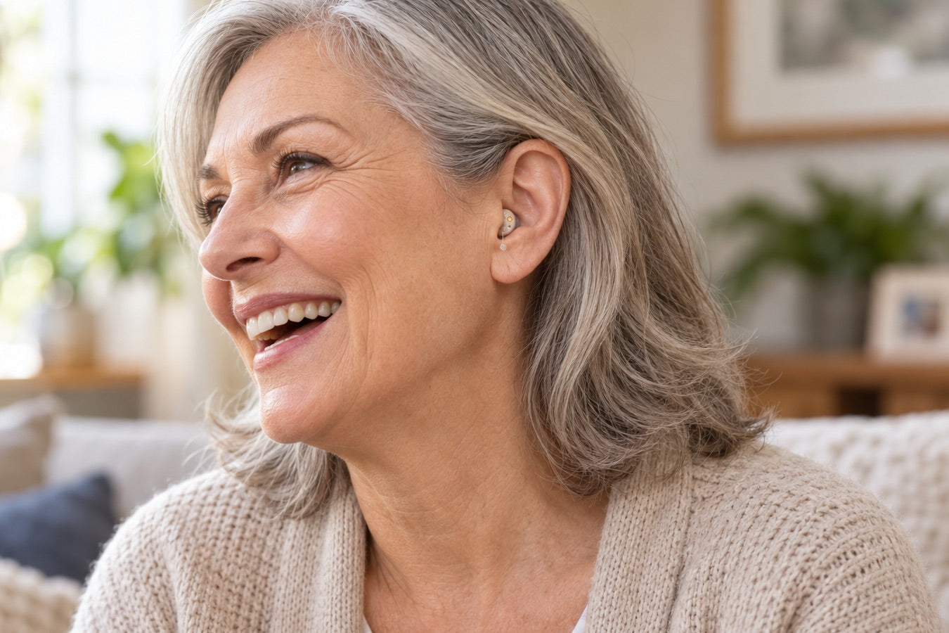 A laughing woman in her sixties wearing an Oricle Pro deep in her ear, its clear pull-wire just visible