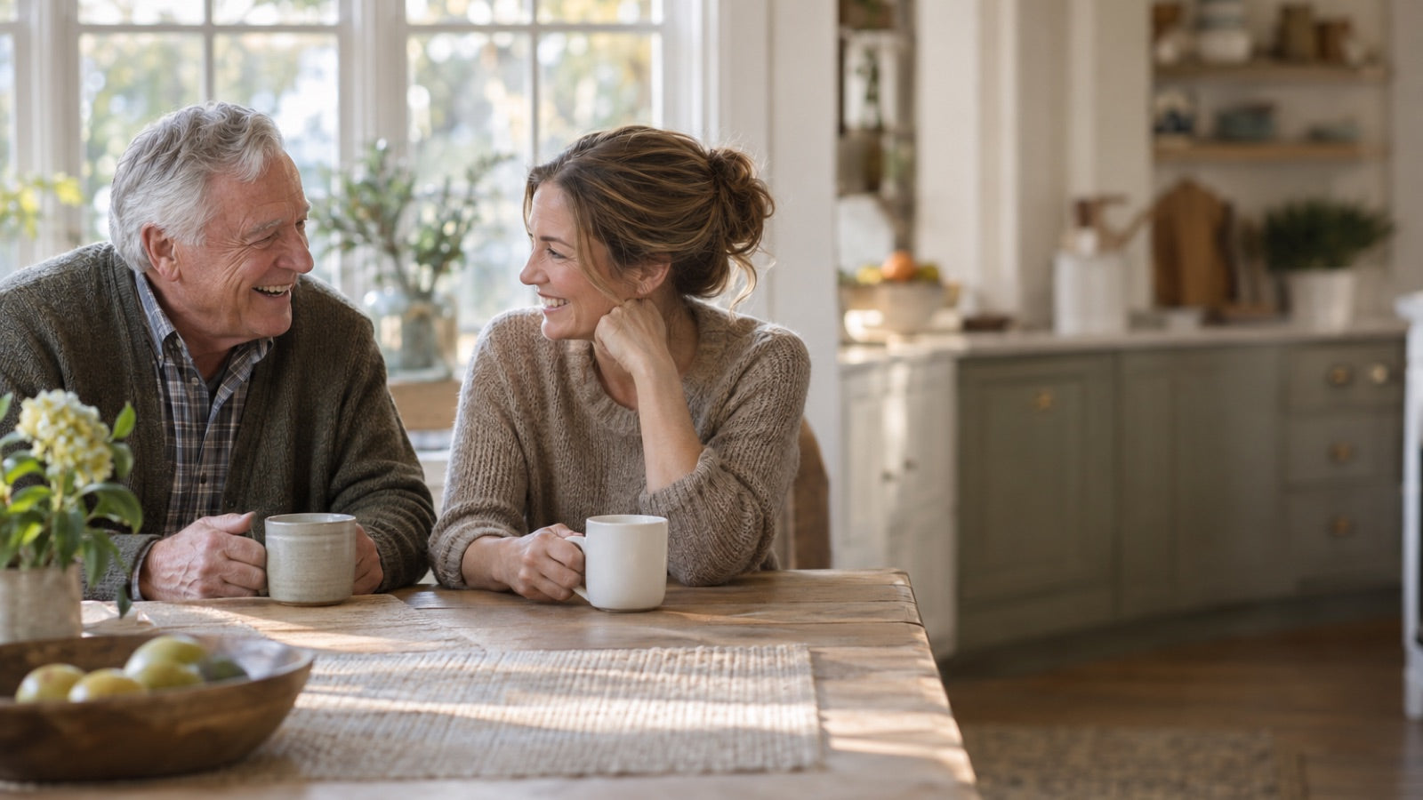 A father laughing with his adult daughter at a sunlit kitchen table
